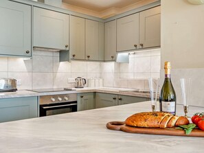 A kitchen with light blue cabinets, a marble countertop, a stove, a kettle, a loaf of bread, a bottle of wine, and glasses. - 2 Bed in Tenby (oc-fb163) (Tenby)