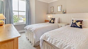 Hotellihuone, jossa on kaksi sänkyä, yöpöytä, lamppu, ikkuna verhoilla ja näkymä ulos.