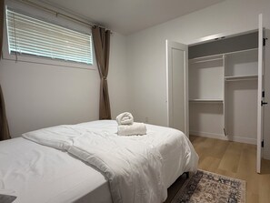 A bedroom with a bed, a window with blinds, a door to a closet, and a rug. - Spacious 2BR Suite|Near WEM|Families|Contractors (Edmonton)