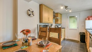 A compact kitchen with wooden cabinets, a dining table set for two, and a small island. - 1 Bed in Tenby (oc-fb162) (Tenby)