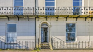 A two-story building with a central entrance, a balcony with ornate metal railings, and a window with a blue curtain. - 1 Bed in Tenby (oc-fb162) (Tenby)