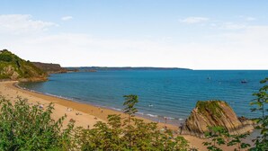 A beach with clear blue water, sandy shore, and rocky cliffs. - 1 Bed in Tenby (oc-fb162) (Tenby)