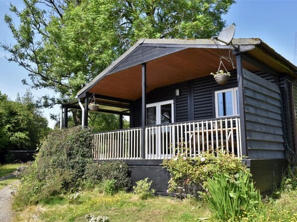 A wooden cabin with a porch, a satellite dish, and a hanging basket.