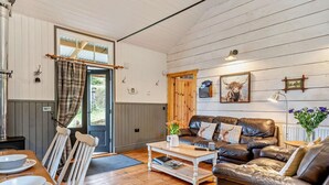 A cozy living room with a wooden floor, a leather sofa, a coffee table, and a dining area with chairs and a table. - 2 Bed in Abergavenny (oc-bn246) (Pantygelli)