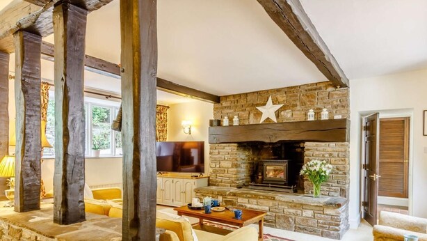 Ein gemütliches Wohnzimmer mit Kamin aus Stein, Holzbalken und einem Fernseher.