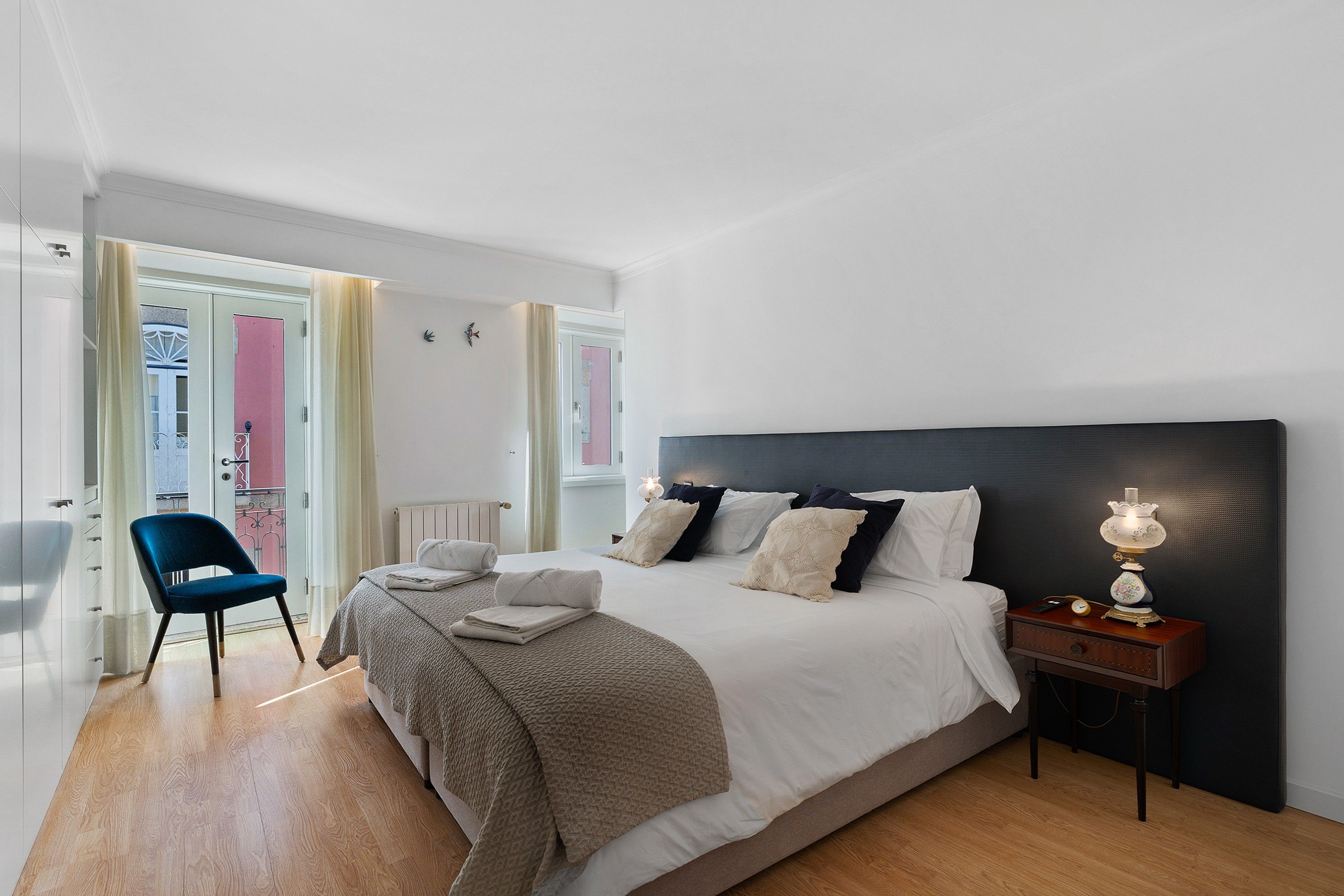 A bedroom with a bed, bedside table, lamp, and a chair.