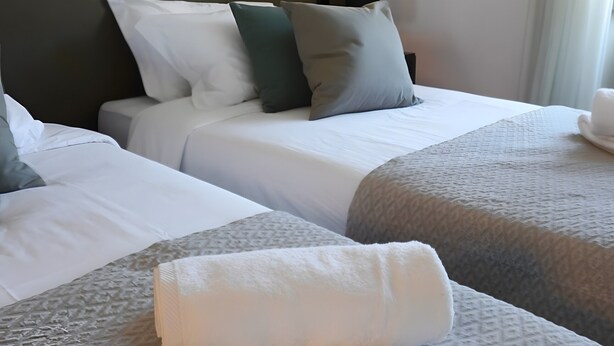 A hotel room with two beds, a headboard, and a nightstand with a lamp. - Casa de São Roque 1 – Beachfront Apartment for 6 Guests (Vila do Conde)