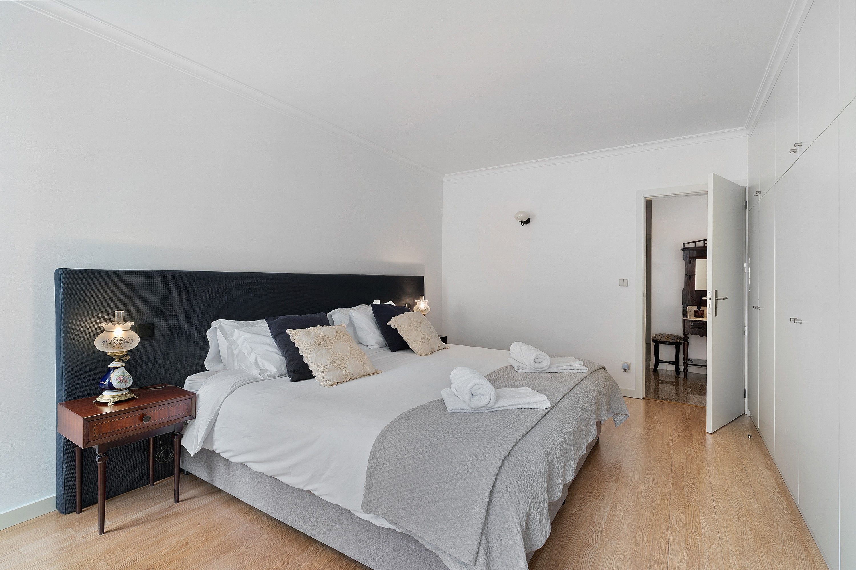 Un dormitorio moderno con cama, mesita de noche, lámpara y vistas al pasillo.