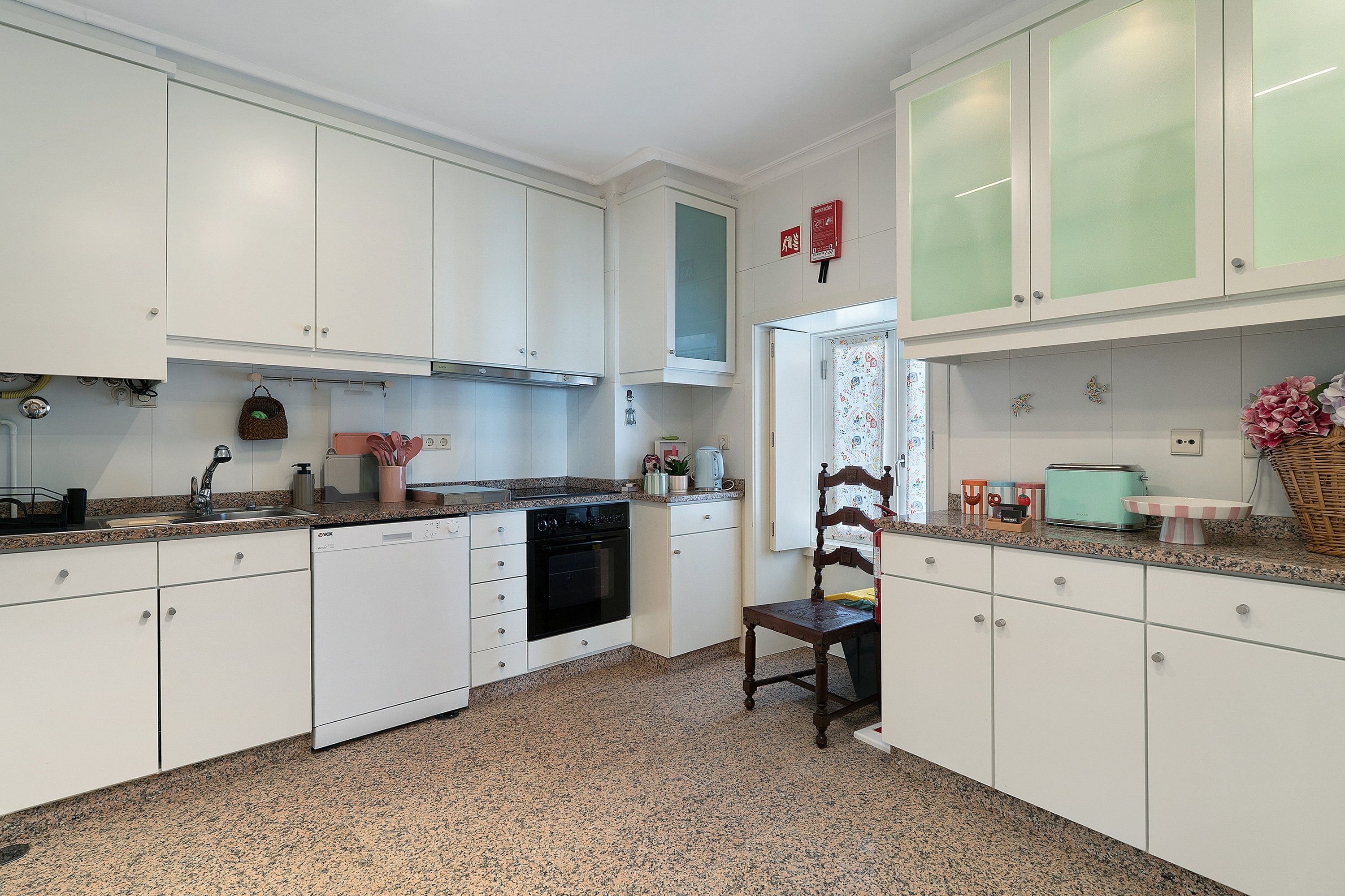 A kitchen with white cabinets, a built-in oven, and a dining area with a chair.