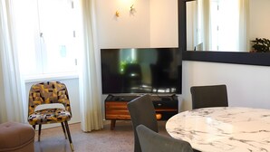 A modern living room with a TV, a round marble table, and a patterned chair. - Casa de São Roque 1 – Beachfront Apartment for 6 Guests (Vila do Conde)