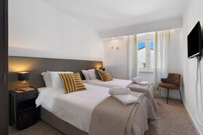 Une chambre d’hôtel avec deux lits, une télévision, une chaise et une fenêtre avec des rideaux.