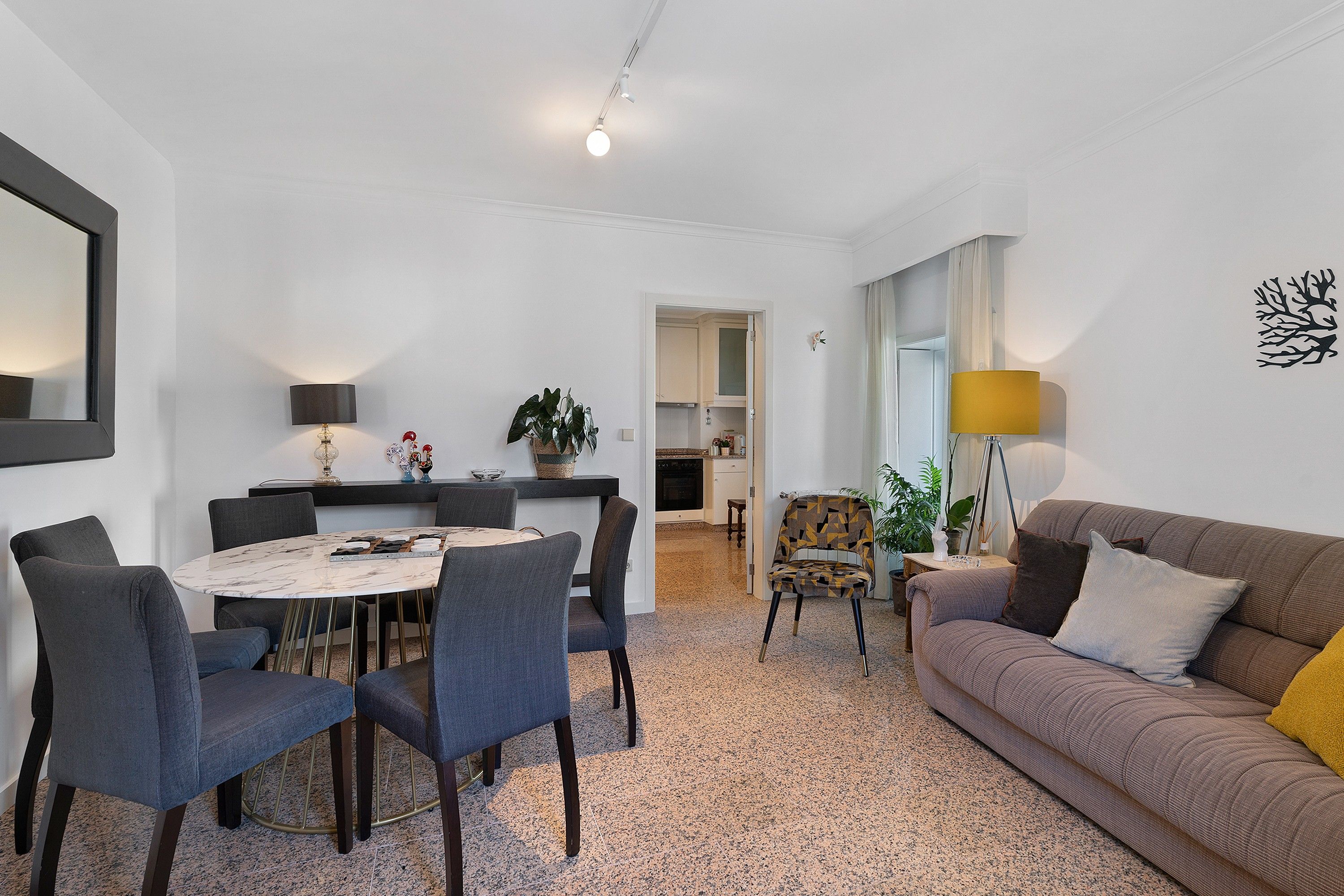 A modern living room with a dining area, a sofa, and a kitchen in the background.