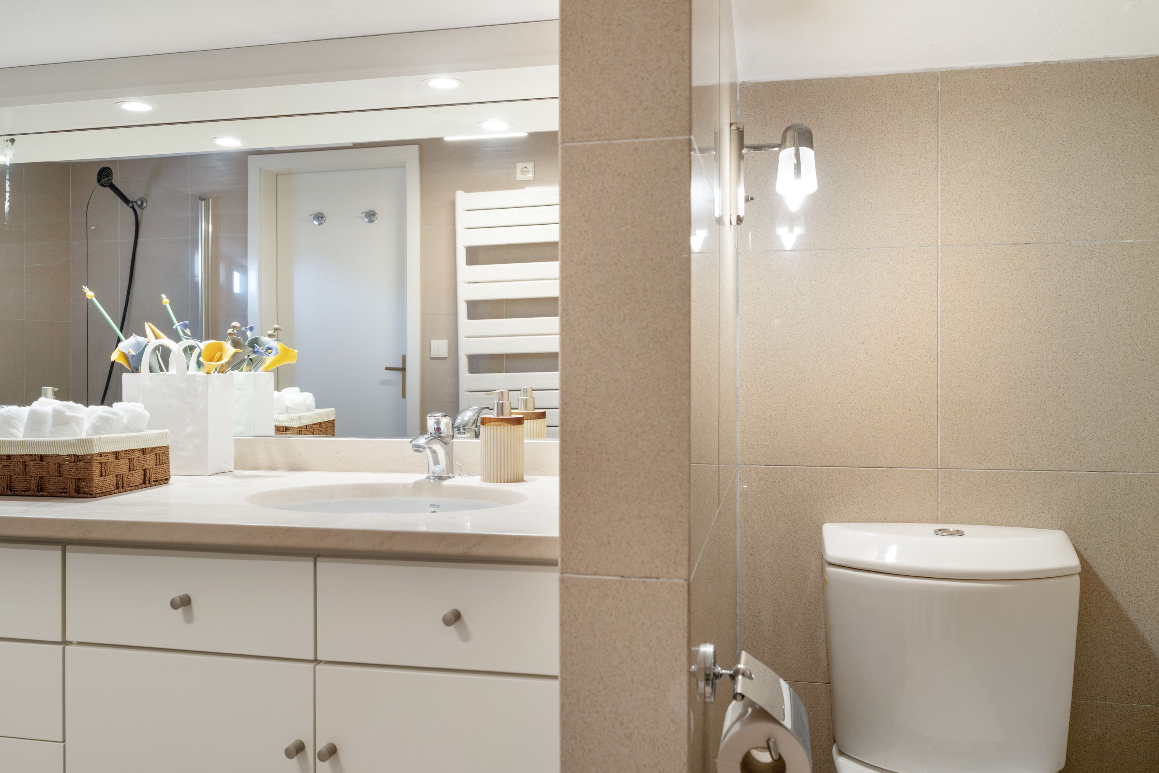 A bathroom with a large mirror, a sink, a toilet, and a cabinet with drawers.