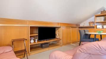 A cozy living room with a flat-screen TV, wooden cabinets, a small table, and a chair.