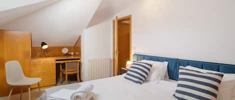 A bedroom with a bed, bedside table, lamp, chair, desk, and a radiator.