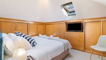 A hotel room with a bed, a television, a chair, and a skylight.