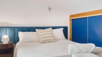 Un lit avec une literie blanche et des oreillers à rayures, une lampe de chevet et une table de chevet en bois.