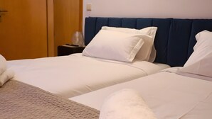 Habitación de hotel con dos camas, una puerta de madera, una mesita de noche y una toalla enrollada sobre la cama.