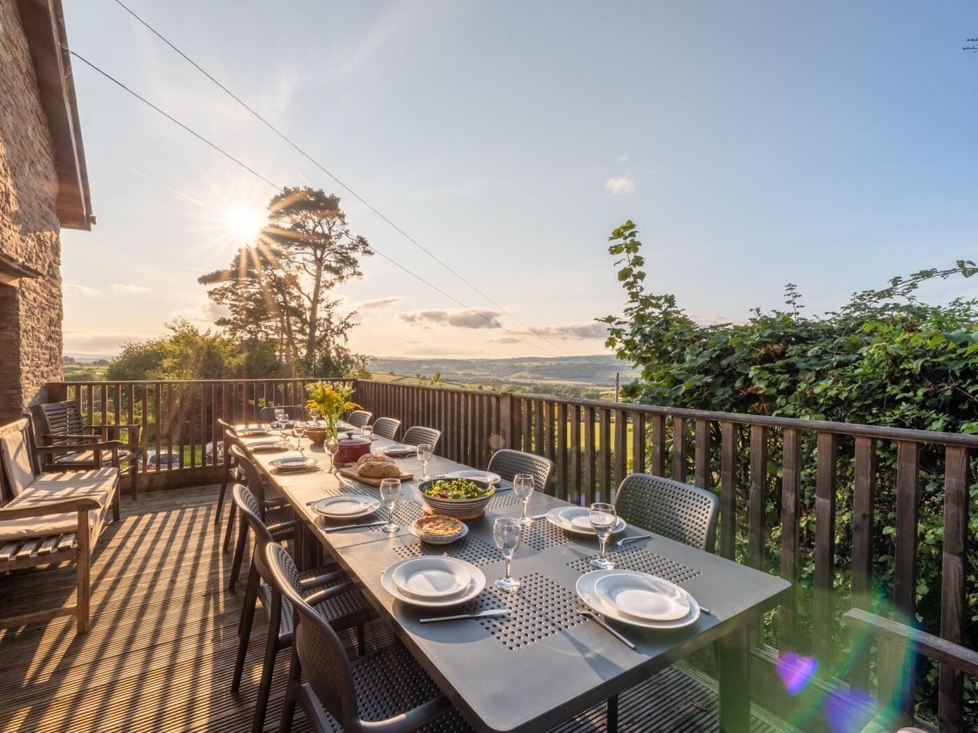 Un área de comedor al aire libre con una mesa dispuesta para cuatro personas, rodeada de sillas y con vistas al paisaje.
