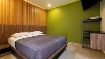 Un dormitorio moderno con cama, cabecera de madera con listones, pared verde y televisor de pantalla plana montado en la pared.