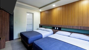 A hotel room with two beds, a wooden panel wall, a door, and a flat-screen TV.