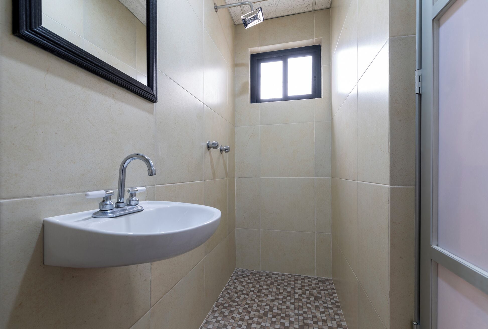 Un baño con lavamanos, espejo, ducha y suelo de baldosas.