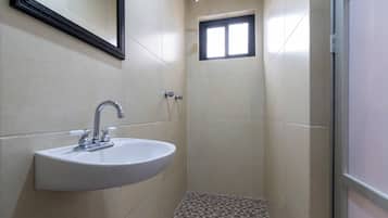Un baño con lavamanos, espejo, ducha y suelo de baldosas.
