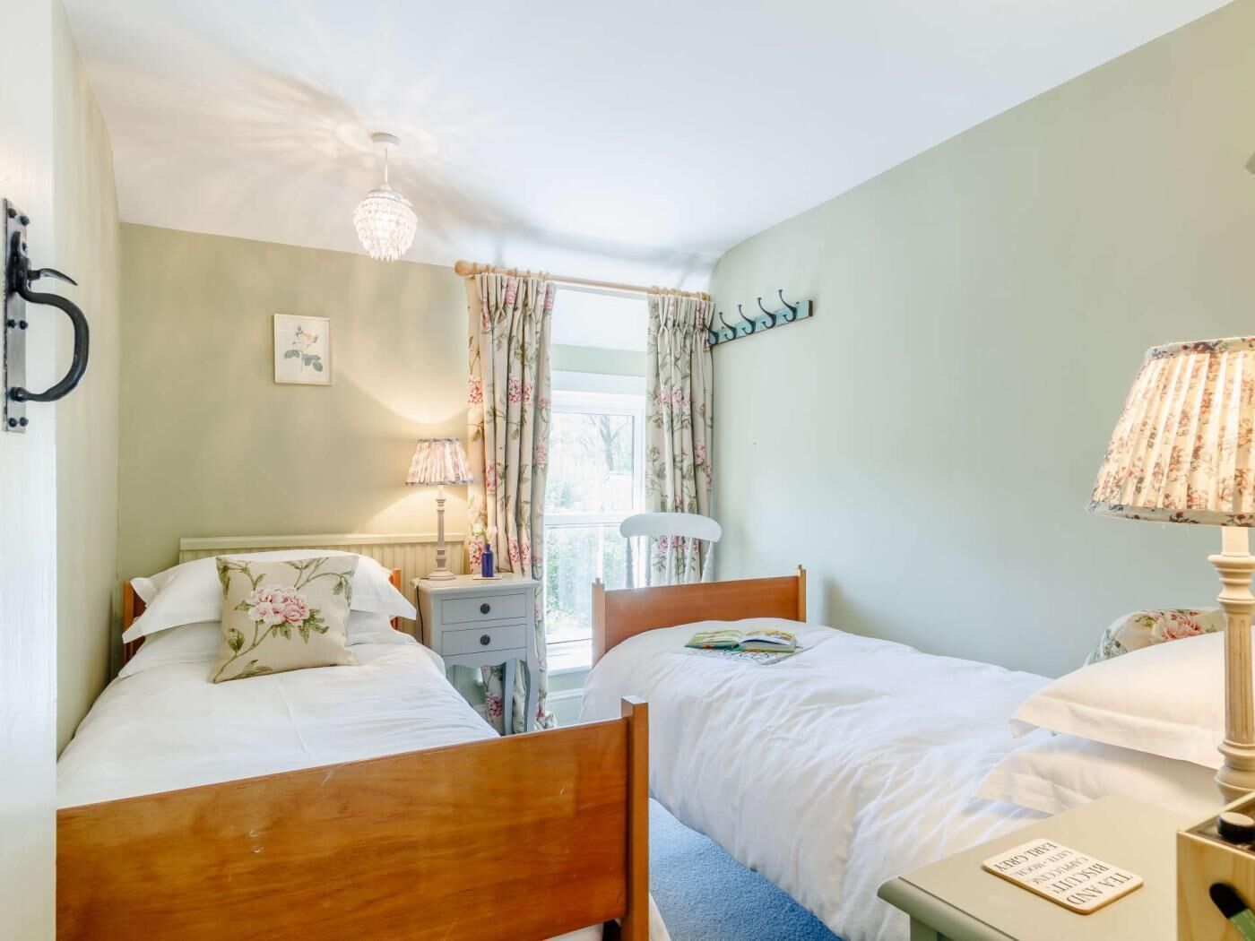 Une chambre avec deux lits, une table de chevet, une lampe, une fenêtre avec des rideaux et un lustre.
