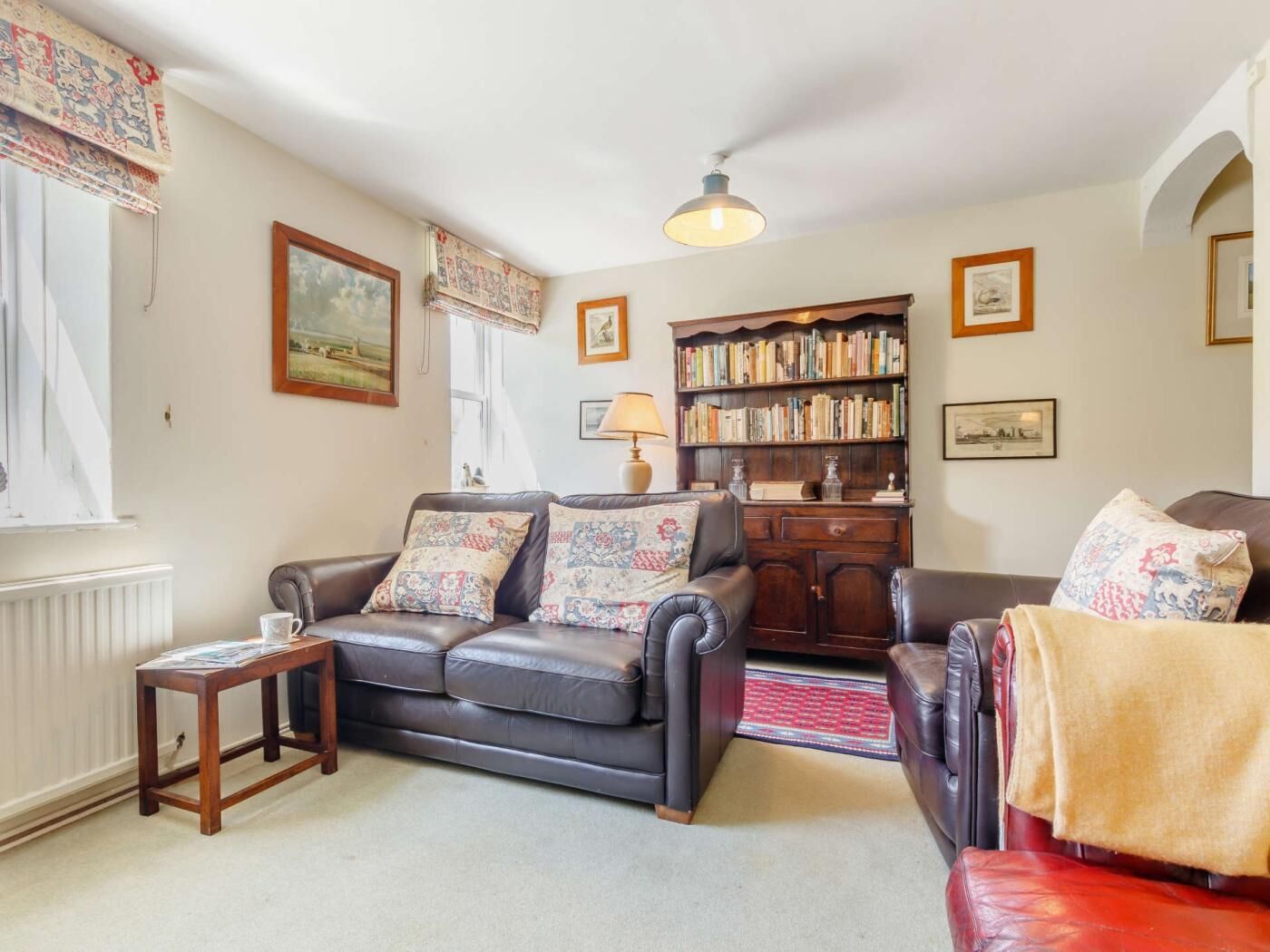 A living room with a dark leather sofa, a wooden coffee table, a bookshelf, and a radiator.