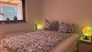 Een slaapkamer met een bed, kussens, een nachtkastje, een wereldbol en een raam met uitzicht op bomen.