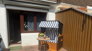 Een terras met een houten bankje, een klein rond tafeltje en een gestreepte luifel.
