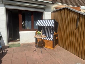 Eine Terrasse mit einer hölzernen Bank, einem kleinen runden Tisch und einem Streifen-Markise.