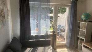 Een woonkamer met een bank, een boekenkast, een wereldbol en een schuifdeur die uitkomt op een terras.