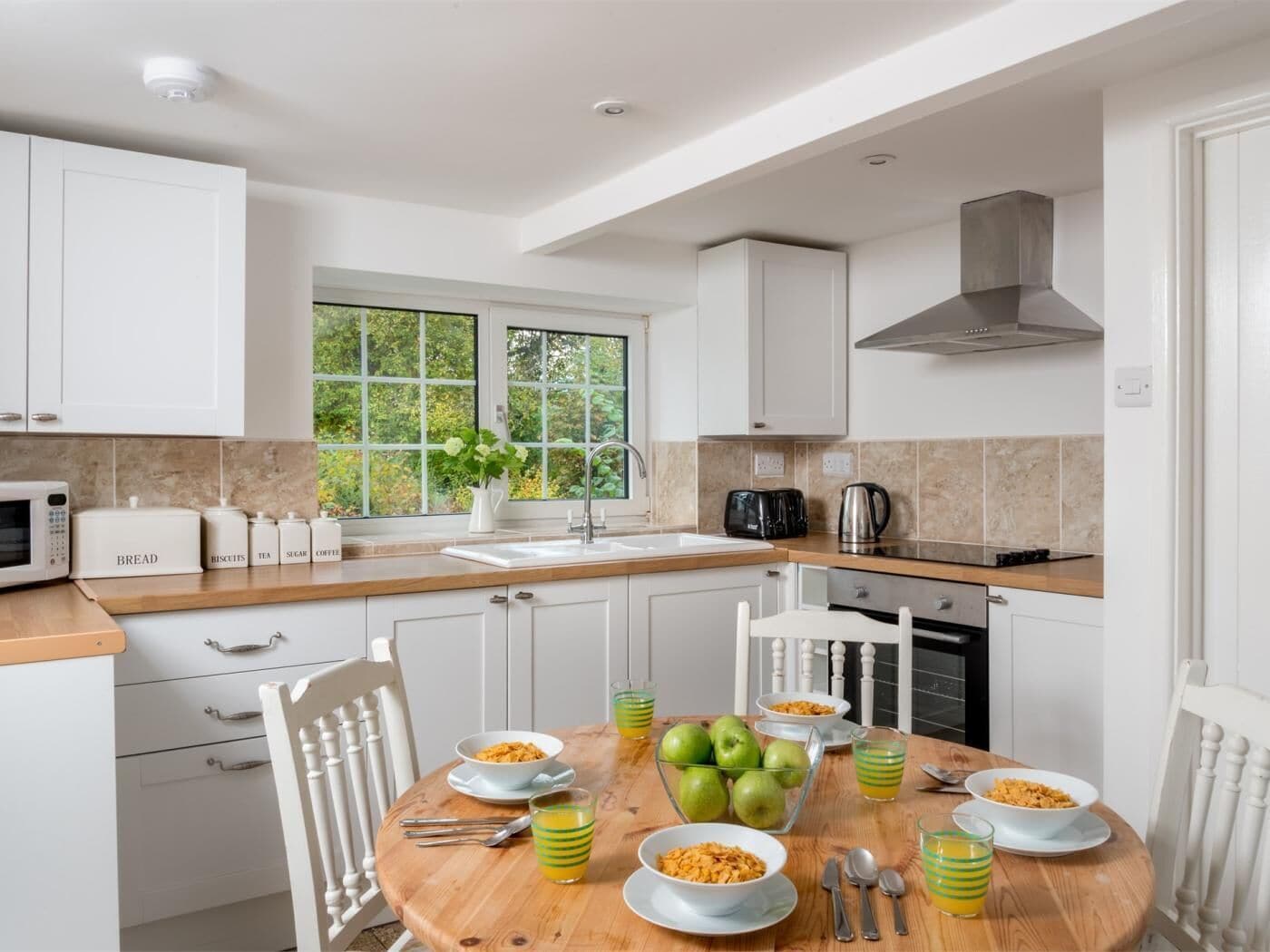A modern kitchen with white cabinets, a wooden countertop, and a dining table set with breakfast items.