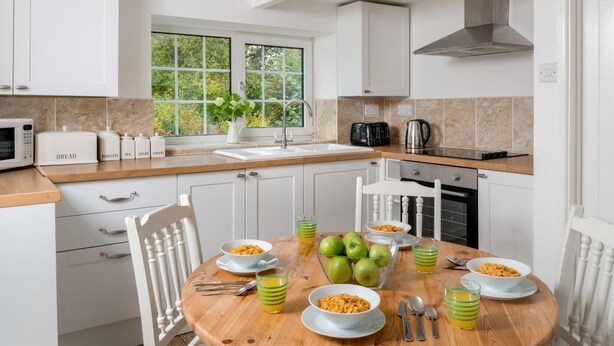 Une cuisine moderne avec des meubles blancs, un plan de travail en bois et une table à manger dressée pour le petit-déjeuner.