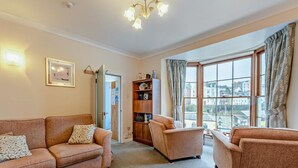 A living room with a sofa, armchair, and a bookshelf. - 1 Bed in Tenby (oc-fb125) (Tenby)