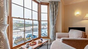 A hotel room with a large window offering a view of the city, a small table with pastries, and two sofas. - 1 Bed in Tenby (oc-fb125) (Tenby)