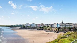 A coastal town with a sandy beach, buildings along the shore, and a prominent church spire. - 1 Bed in Tenby (oc-fb125) (Tenby)