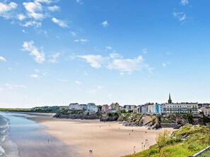 A coastal town with a sandy beach, buildings along the shore, and a prominent church spire. - 1 Bed in Tenby (oc-fb125) (Tenby)