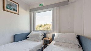 Quarto com duas camas, janela com vista, quadro na parede e sinal de saída de incêndio.