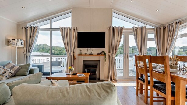 A modern living room with a sofa, a dining table with chairs, a fireplace, and large windows with curtains. - 3 Bed in Stepaside (oc-fb132) (Stepaside)