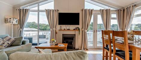 A modern living room with a sofa, a dining table with chairs, a fireplace, and large windows with curtains.