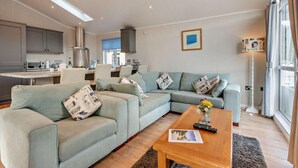 A modern living room with a sectional sofa, a coffee table, and a kitchen in the background. - 3 Bed in Stepaside (oc-fb132) (Stepaside)