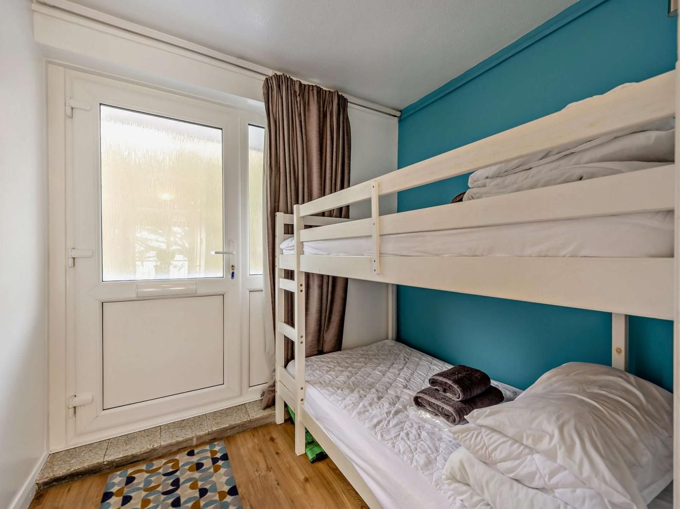 A room with a bunk bed, a door with a frosted window, and a patterned rug on the floor.
