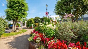 Ein Gartenpfad mit verschiedenen Blumen und Bäumen, einer Lampe und einer Bank.