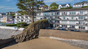 Ein Küstengebäude mit mehreren Balkonen, einem Sandstrand und einer felsigen Klippe.