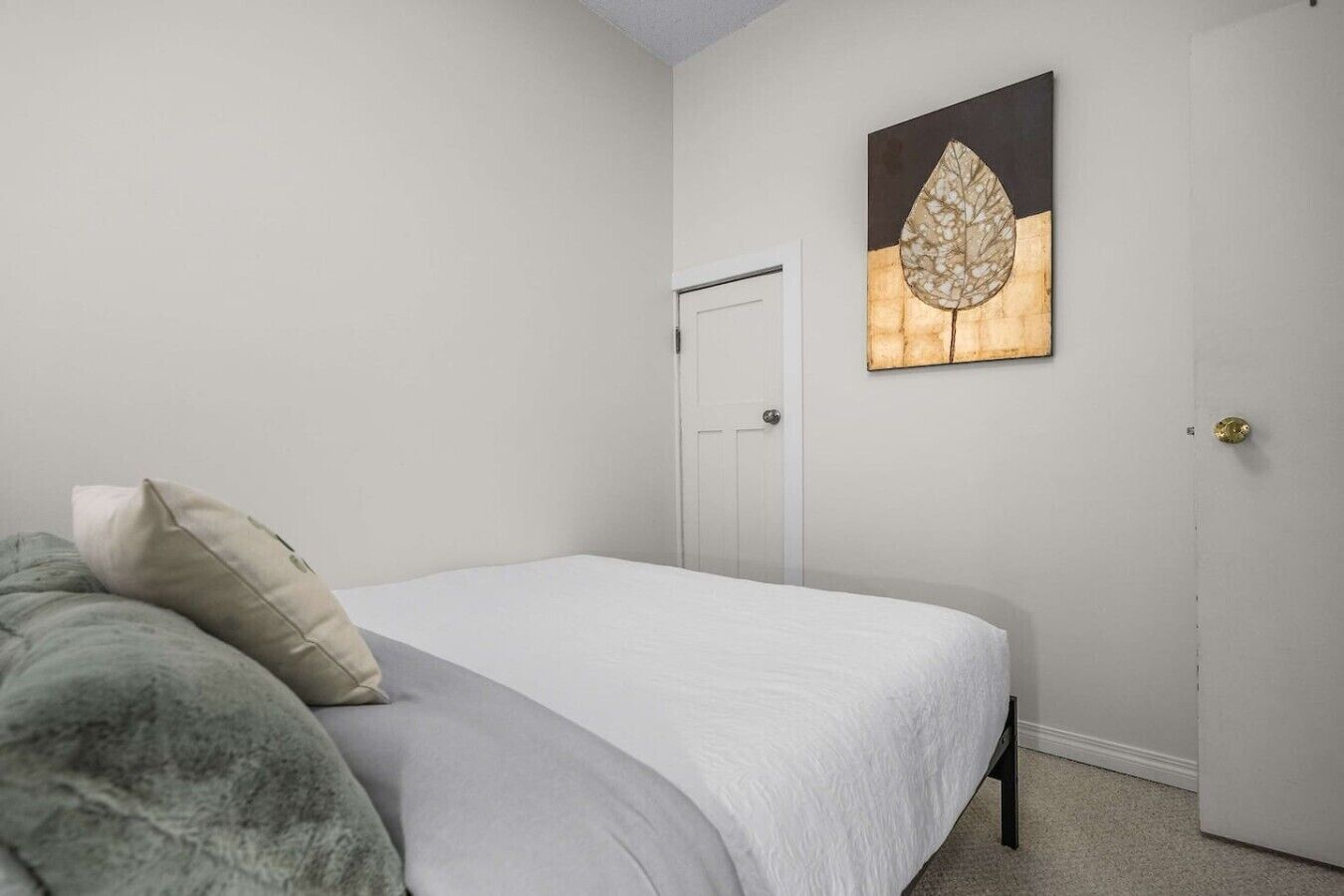Un dormitorio con cama, almohadas, una puerta y una obra de arte en la pared.