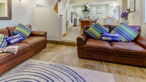 A living room with two brown leather sofas, a wooden floor, a staircase, and a kitchen in the background. - 4 Bed in Tenby (oc-fb042) (Tenby)