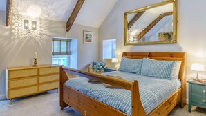 A bedroom with a wooden bed, a dresser, a mirror, and a ceiling light fixture. - 4 Bed in Tenby (oc-fb042) (Tenby)
