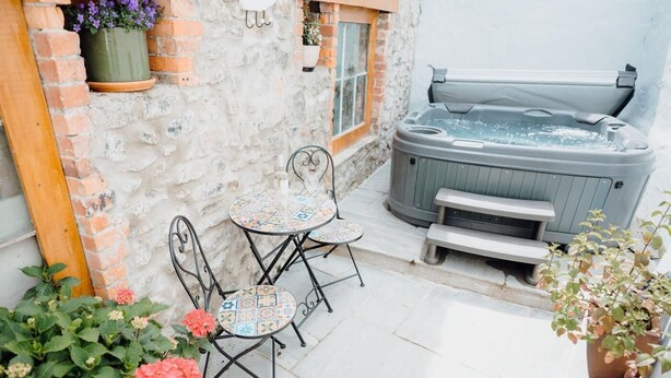 A patio with a hot tub, two metal chairs, a small table, and potted plants. - 4 Bed in Tenby (oc-fb042) (Tenby)